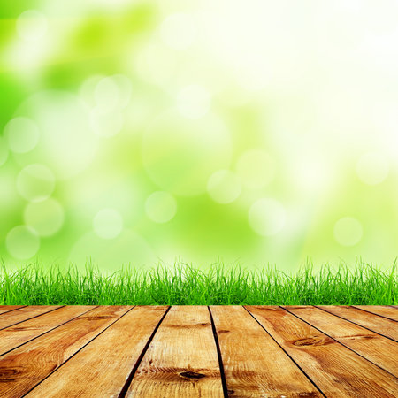 Fresh spring green grass with green bokeh and sunlight and wood floor. Natural backgroundの写真素材