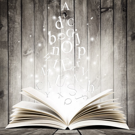 Open book with flying letters over wooden background. Magic bookの写真素材