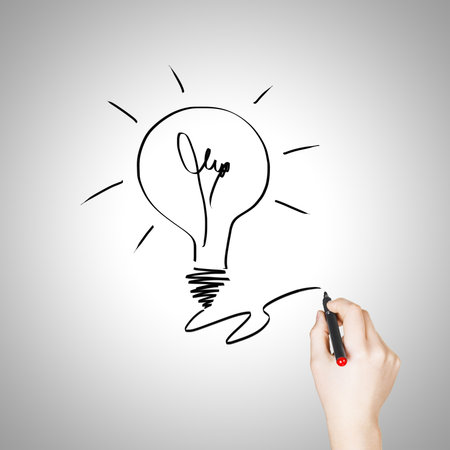 Female hand drawing light bulb over white backgroundの写真素材