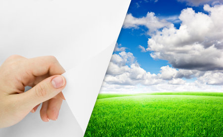 Blank sheet of paper with hand opening it. Over field nature backgroundの写真素材