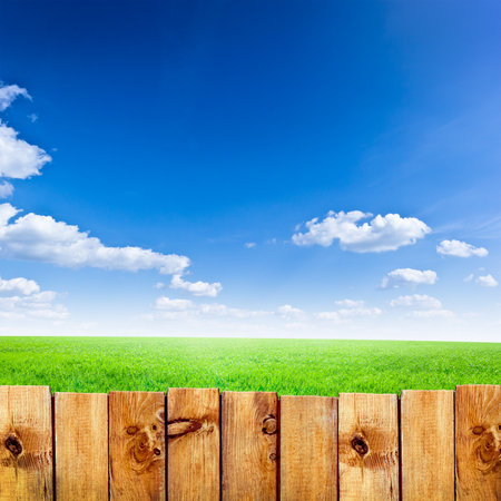 Wooden fence against green field and blue sky backgroundの写真素材