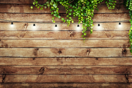 Garland lamps over wooden board fence with green leaves. Decoration backgroundの写真素材