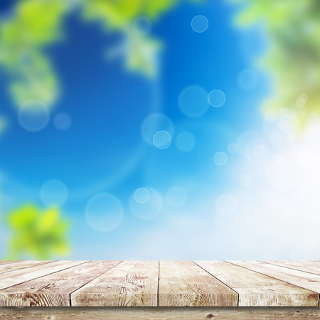 Fresh spring green leaves with blue bokeh and sunlight and wood floor. Natural backgroundの写真素材