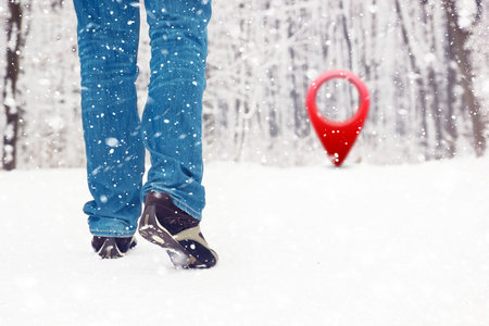 Man walking in winter snow covered forest with red location pinの写真素材