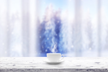 Cup with hot drink on wooden table and window over winter snow covered forest backgroundの写真素材