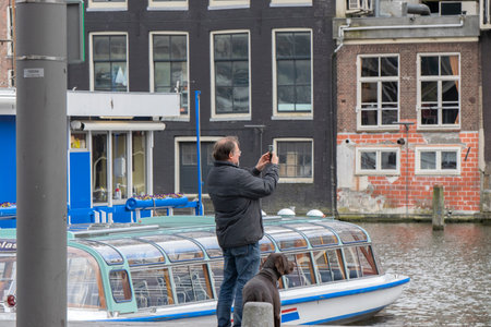 Man And Dog Taking Pictures At The Canal Cruise Boats At The Damrak Street Amsterdam The Netherlands 3 April 2020のeditorial素材