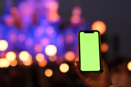 close up hand showing green screen smart phone in amusement park at night. Beautiful bokeh...