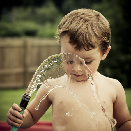 Boy plays with hose, creating water window. の写真素材