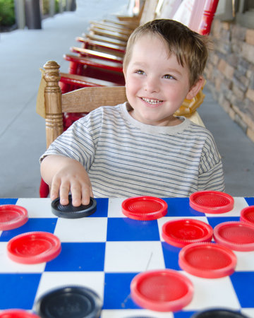 Smiling young boy playing checkers while sitting on rocking chair on porchの写真素材