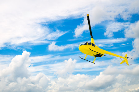 Yellow helicopter flying with cloudy blue sky backgroundの写真素材