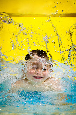 Young boy or kid has fun splashing into pool after going down water slide during summer with copy space の写真素材