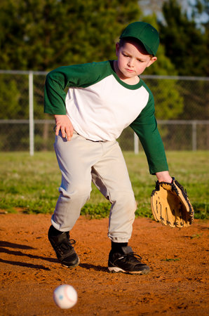 Young child fielding ball while playing baseballの写真素材