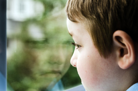 Sad child looking out window on gloomy dayの写真素材