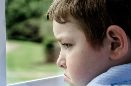 Sad child looking out window on gloomy dayの写真素材