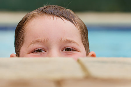 Portrait of child peeking over edge of pool while swimmingの写真素材
