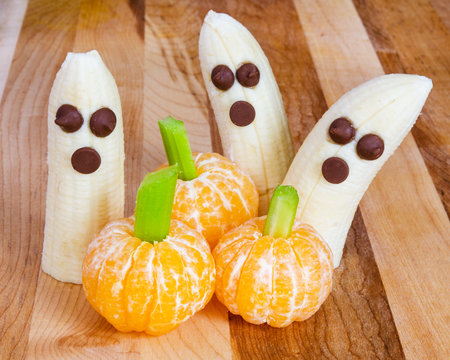 Halloween child friendly treats with bananas and clementines made to look like pumpkins and ghostsの写真素材