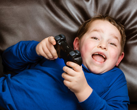 Young boy playing video game laying on couch at home