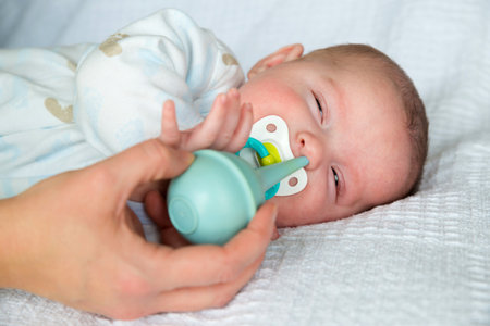 Mother using bulb syringe to clean unhappy infant baby s noseの写真素材