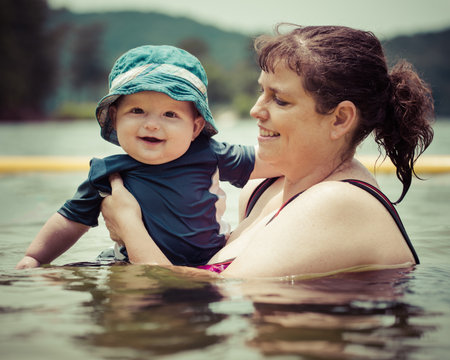 Mother teaching infant baby son to swim in lake during summer in vintage filtered imageの写真素材