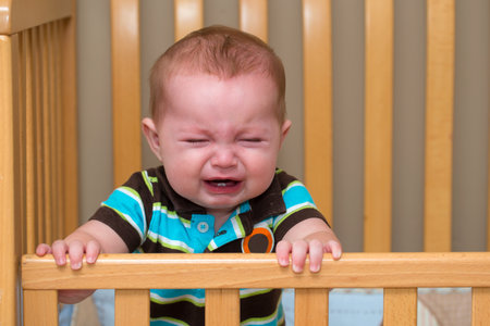 Crying unhappy baby standing in his cribの写真素材