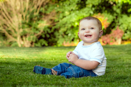 Smiling happy baby playing on the grass outdoorsの写真素材