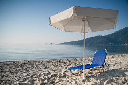 Deckchair under white umbrella. Blue sky and water.の写真素材