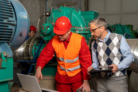 Young Technician with Laptop Computer Checking Data With Technical Manager in Mechanical Room. Portrait of Young Worker in District Heating Power Plant. Digital Technology Concept. Industry 4.0 .の写真素材