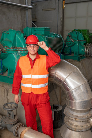 Young Technician in Red Coveralls and Hardhat Standing in Industrial Interior With Pipes and...