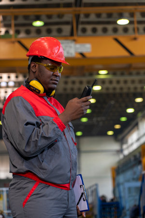 African American Worker In Protective Workwear Talking On Radio Communication Equipment In A...