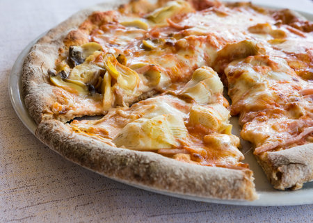 In the pictured a cut pizza with tomato, mozzarella, mushrooms, ham and artichokes.の写真素材