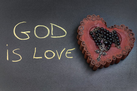 In the picture a rosary iron placed over a heart of red wax, on the left side the inscription "God is Love" made with a crayon.の写真素材
