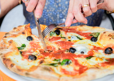 Close-up of woman hands cutting pizza outside at restaurant, selective focus.の写真素材