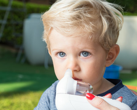 Mother using baby electric nasal aspirator. She is doing a mucus suction to twenty months baby boy,outdoor.の写真素材