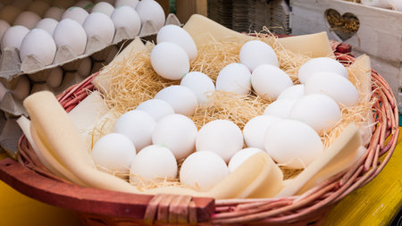 White chicken eggs leaning on straw in wooden basket at market,outdoor.