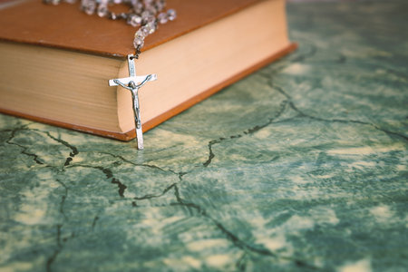 Silver rosary and cross resting on the closed book at green table,front view.religion school concept.Vintage style.の写真素材