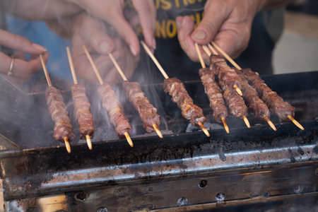 Man cooking marinated meat, Pork meat grilling on wooden skewer, outdoor grill with smoke coming up from the fire below. close upの写真素材