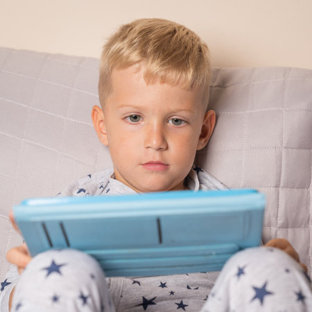Caucasian baby boy using digital tablet while lying on bed at home,front view