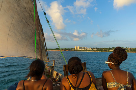 Three african american girls sitting on the boat looking towards the beach in front of...