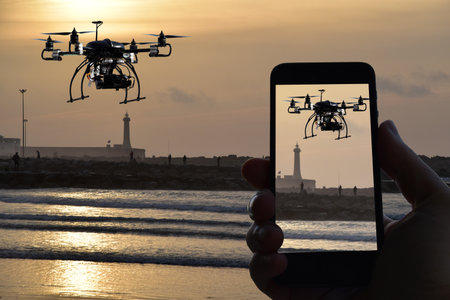 Drone, remote control from smartphone, sunset over the sea whit watchtower backgroundの写真素材