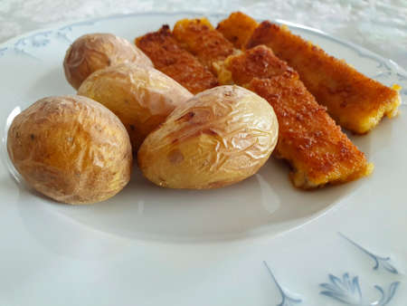 Jacket potatoes with fish sticks on a white plate. Food, close up.の写真素材