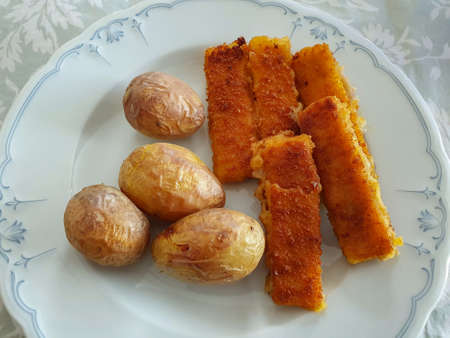 Jacket potatoes with fish sticks on a white plate. Food, close up.の写真素材