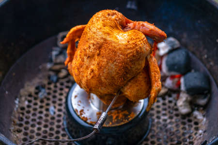 Marinated chicken on a chicken holder with thermometer on a barbecue with glowing charcoals. Close-up during a barbecue in the garden.の写真素材