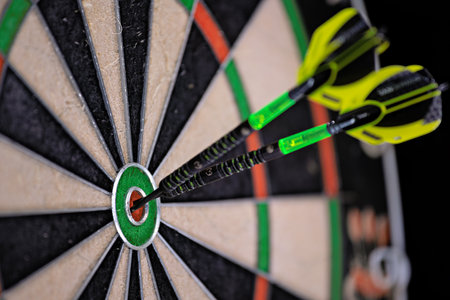 Two black and green darts stuck in the bullseye of a dartboard. Close up of a dartboard.の写真素材
