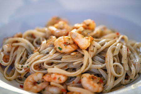 Linguine aglio e olio with cooked shrimp, garlic and herbs served on a white plate. The pasta is prepared with olive oil and seasoning. Horizontal composition. Suitable for restaurant menus, food blog articles or culinary advertising content.の写真素材
