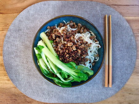 Top view of egg noodles served with fried minced meat and fresh bok choy. Traditional Asian dish with chopsticks on a wooden table.の写真素材