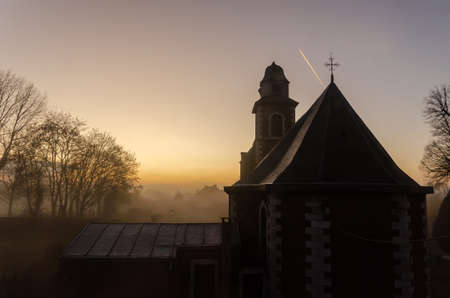 A church with fog during sunset and a plane passing byの写真素材