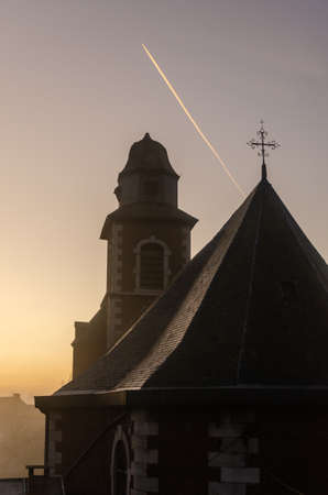 A church with fog during sunset and a plane passing byの写真素材