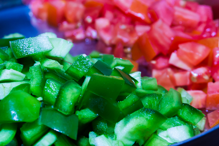 Close up sliced green capsicum in a plate with sliced red tomato out of focusの写真素材