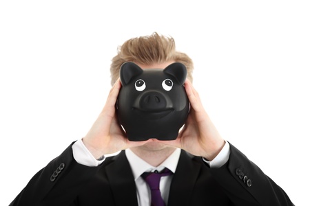 Businessman holding a piggybank in front of face. Wearing a black suit with a purple tie. White background.の写真素材
