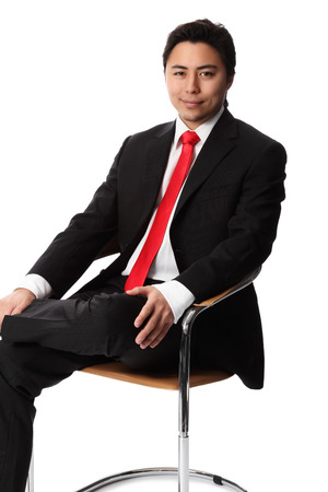 Young serious businessman sitting down in a chair wearing a suit and red tie  White background の写真素材